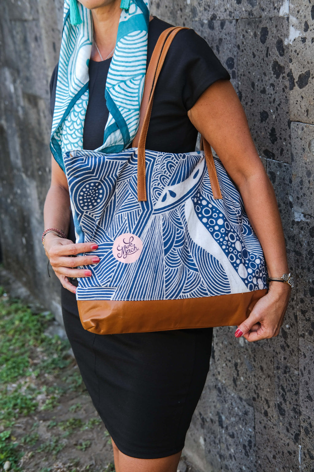 Model wearing the LeMerch TENCEL™ Square Scarf wrapped in her head and holding the LeMerch tote bag featuring an original artistic print.