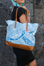 Model holding the LeMerch tote bag and wearing the LeMerch TENCEL™ Square Scarf wrapped in her head and featuring an original artistic print.