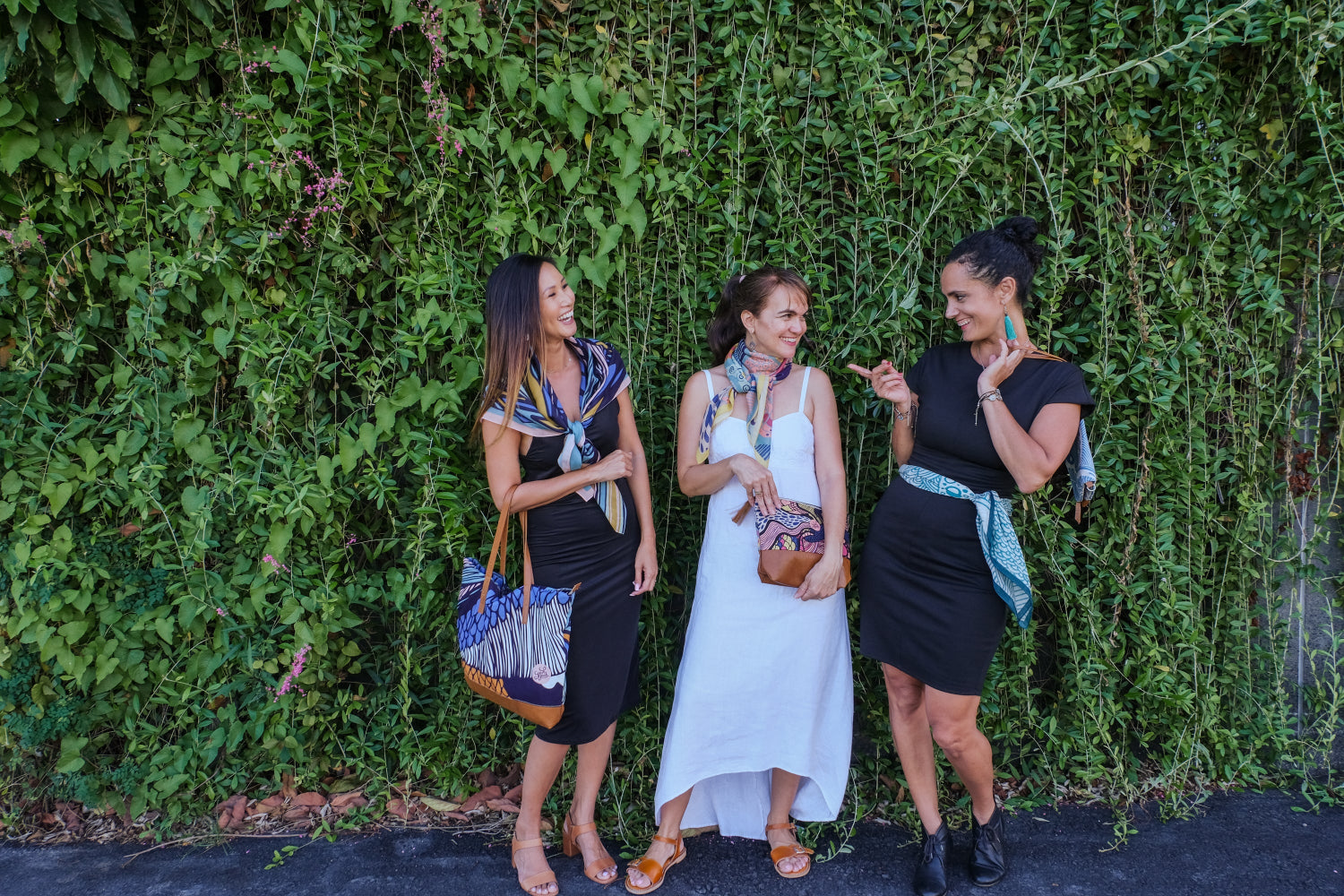 Three women wearing LeMerch scarves and carrying handcrafted tote bag, clutch and pouch from LeMerch