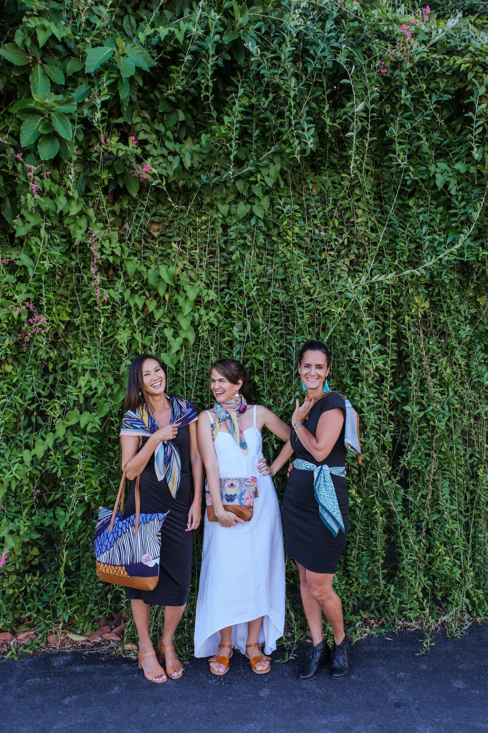 Three women wearing LeMerch scarves and carrying handcrafted tote bag, clutch and pouch