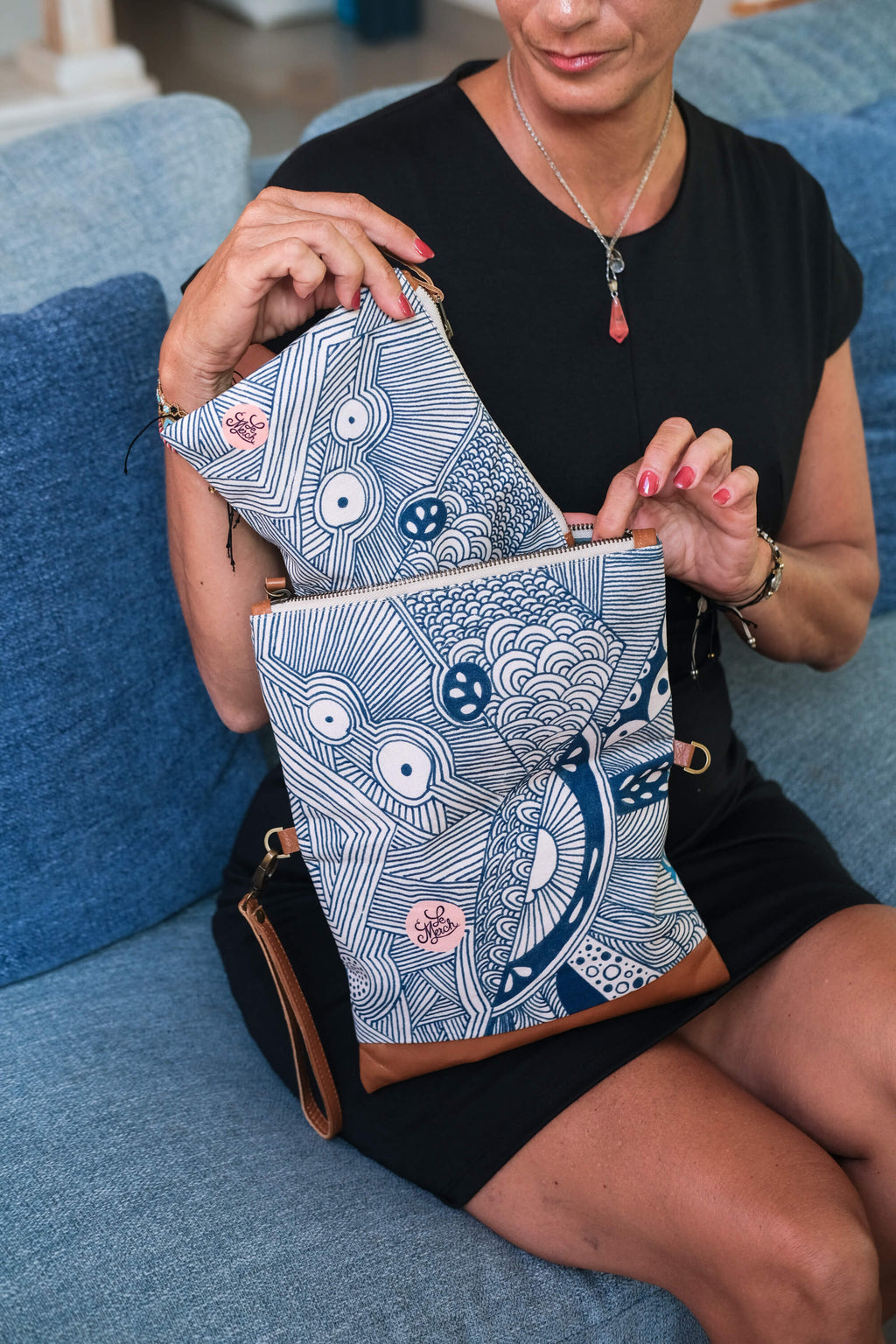Model opening the LeMerch Clutch to showcase a small pouch and its spacious interior and original artistic print with leather details and strap