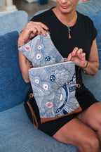 Model opening the LeMerch Clutch to showcase a small pouch and its spacious interior and original artistic print with leather details and strap